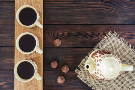 Three cups of coffee, coffee pot and chocolate candies on a light board on a dark wooden backgroundの写真素材