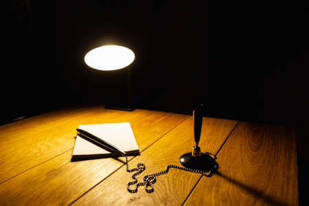 Notepad and pen on a wooden table in the light of a table lampの写真素材