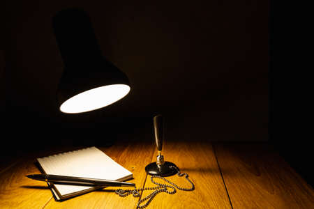 Notepad and pen on a wooden table in the light of a table lampの写真素材