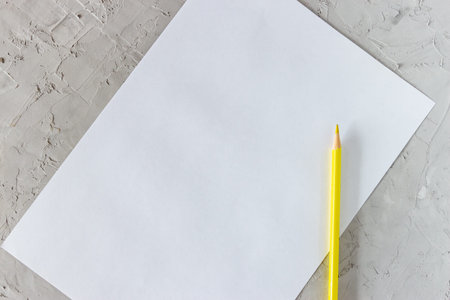 Yellow pencil and blank sheet of white paper on gray concrete background