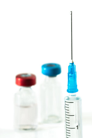 Medical needle with a drop of vaccine against the background of vaccine vialsの写真素材