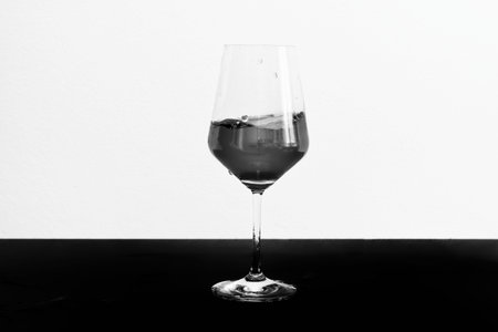 Black and white photo of red wine in motion in a glass on dark table and white background