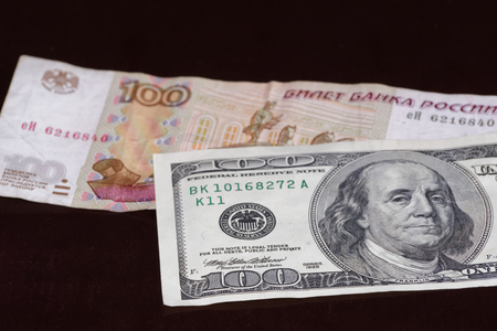 One hundred american dollars banknote is above russian one hundred rubles on black backgroundの写真素材