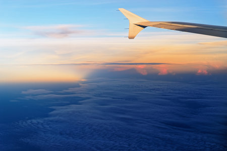 Airplane wing in sunlight against sky in sunset colors. View from porthole
