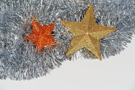 Christmas decoration from two stars in orange and golden colors lying in silver tinsel on white...