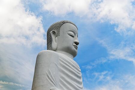 Side view at giant Buddha statue against blue cloudy skyの写真素材