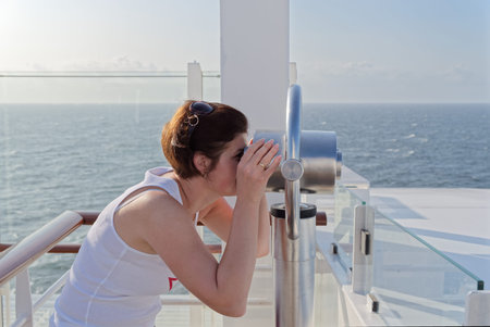 Side view of young woman in white shirt looking through an observation telescope on a ship