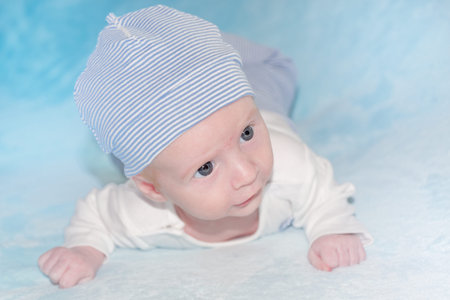 Close-up of 2 months old infant on blue blanket while lying on their tummy and holding head up