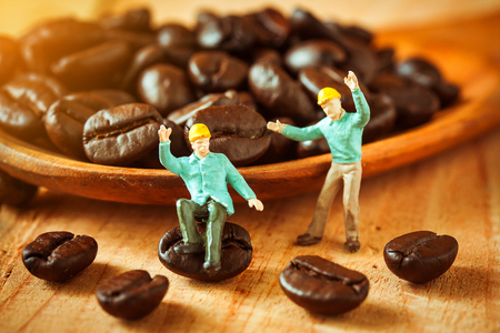 selective focus of miniature worker pointed at coffee bean on wooden spoon,love coffee concept.の写真素材
