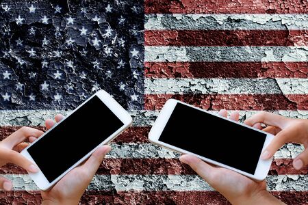 woman hand hold and touch screen on smartphone or cellphone over blurred America flag on clacked wall background.の写真素材