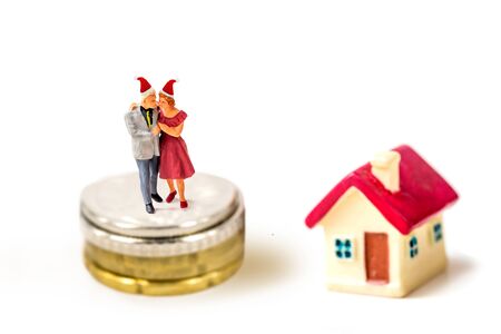 miniature older couple family wear Christmas cap stand on stack coins with tiny home isolate on white background,  Image for Christmas and holiday home and money  management concept.の写真素材