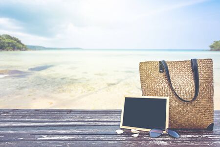 bamboo bag and chalkboard on wooden floor over blurred tropical beach and blue seaの写真素材