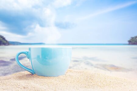 blue cup of coffee on white sand beach over blue sky and sea on day noon light background.の写真素材