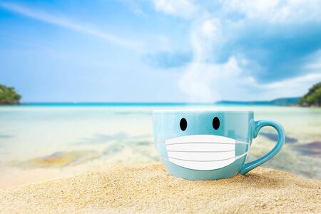 blue cup of coffee on white sand beach over blue sky and sea on day noon light background.の写真素材
