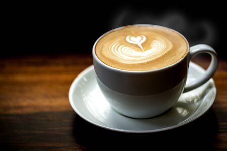 White cup of hot late art coffee on wooden table background.の写真素材