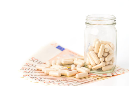 herb capsule pills spilling out off bottle over euro banknote isolated on white background.