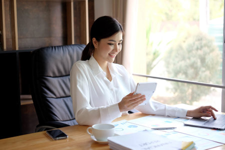 Beautiful asian businesswoman using mobile phone while working in officeの写真素材