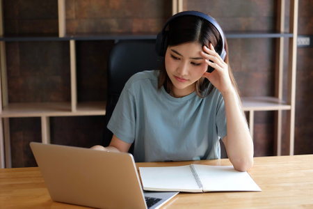 Young asian woman listening to music with headphones and using laptop.の写真素材