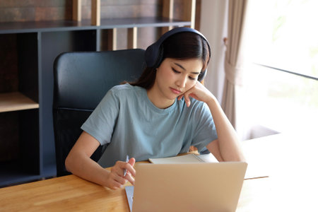 Young woman listening to music with headphones while using laptop computer at homeの写真素材