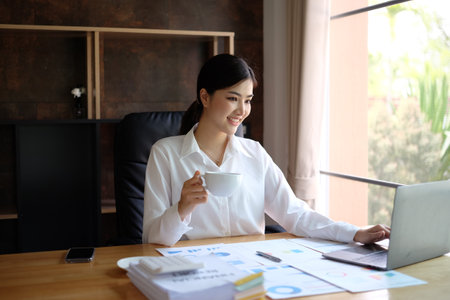 Beautiful asian businesswoman working with laptop and drinking coffee in office.の写真素材