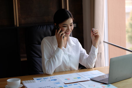 Young businesswoman talking on mobile phone while sitting at office desk.の写真素材