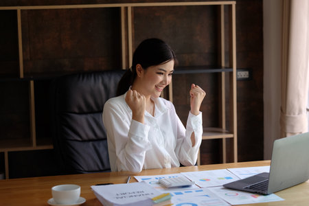 Successful asian businesswoman celebrating success at her workplace in officeの写真素材