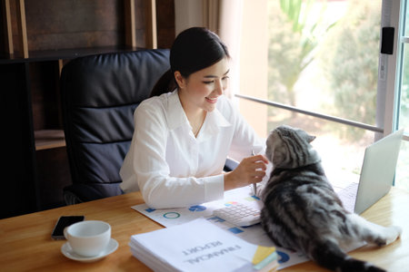 Young businesswoman working with laptop computer in office and cat on table.の写真素材