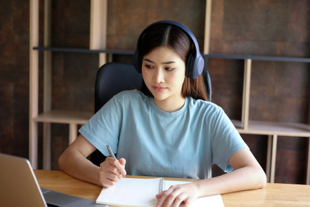 Young asian woman listening to music with headphones and writing in notebook.の写真素材