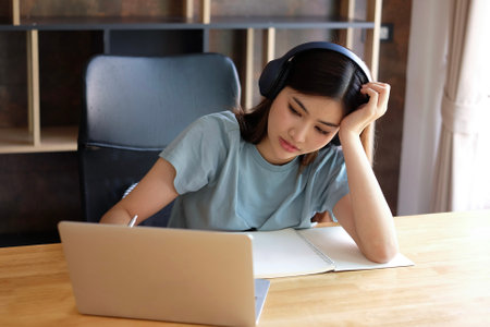 Young Asian woman listening to music with headphones while studying at home.の写真素材