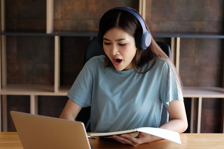 Young asian woman using laptop and listening to music in coffee shopの写真素材