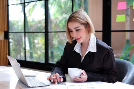 Beautiful businesswoman using laptop and drinking coffee in coffee shop.の写真素材