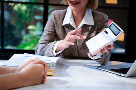 Close-up of businesswoman using calculator while working with colleague in officeの写真素材