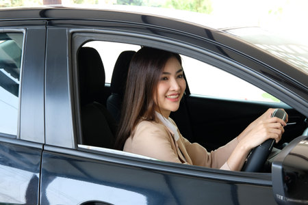 young asian woman driving a car and using her mobile phone.