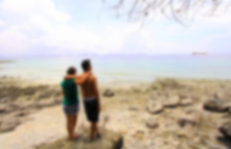 Man and woman standing arm in arm on a rock by the sea,blurred for presentation effect, abstract...