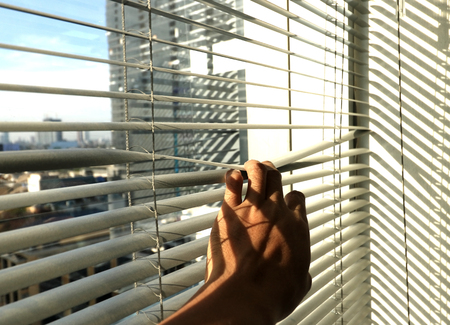 Hand taking a peek through the window blindsの写真素材
