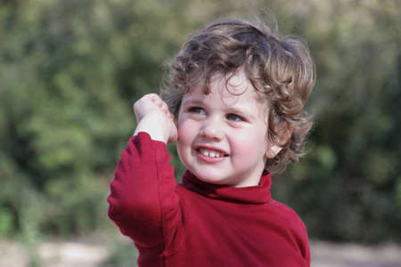Blond boy with curly hair wearing a red vest in the fieldの写真素材