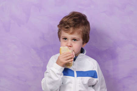 Children dressed in white on a purple background eats a sandwichの写真素材