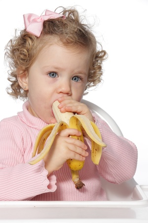 Blue-eyed little girl eating a piece of fruit in front of a white backgroundの写真素材
