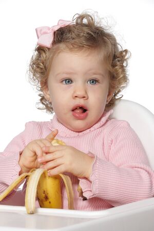 Blue-eyed little girl eating a piece of fruit in front of a white backgroundの写真素材