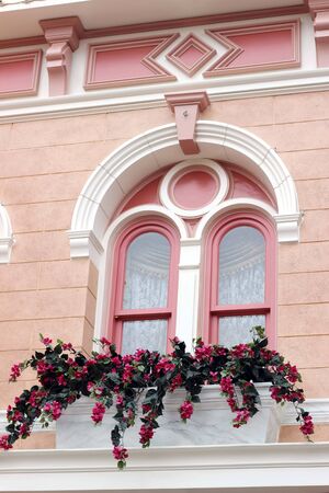 A basket of bright pink and red flowers hangs on the window of a home in an ancient building in France, surrounded by beautiful patterns in the stone wall.の写真素材