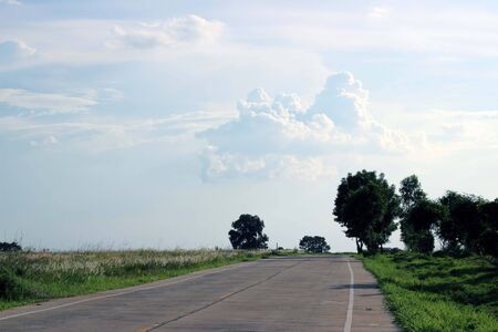 asphalt road through the green field and clouds on blue sky in summer dayの写真素材