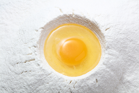 raw liquid egg on heap of wheat flourの写真素材