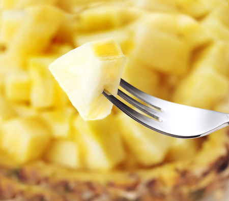 heap of chopped slice of pineapple with one piece on fork on white backgroundの写真素材