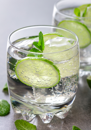 two glasses of alcohol drink with ice, sliced lime and leaves of mint on gray slate backgroundの写真素材