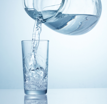 Water is pouring from pitcher into glass on tableの写真素材