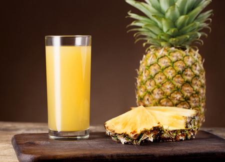 Glass of pineapple juice near whole ripe pineapple on wooden backgroundの写真素材