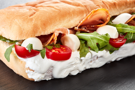 close-up view of sandwich with meat, mozzarella and greens on black slate backgroundの写真素材