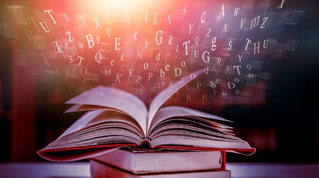 Imagine opening an old book blurred with magic power on the table and the English alphabet floating above the book with magic light as a beautiful background design.の写真素材