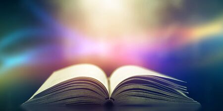 Imagine a picture book of an ancient book opened on a wooden table with a sparkling golden background. With magical power, magic, lightning around a glowing glowing book In the room of darknessの写真素材