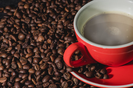 Hot coffee in red cup and coffee beans are the background.
